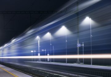 Railway at night. Light trails of passenger train at illuminated railroad station.