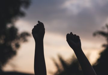 Silhouette of two hands raise with blurred sunset sky background